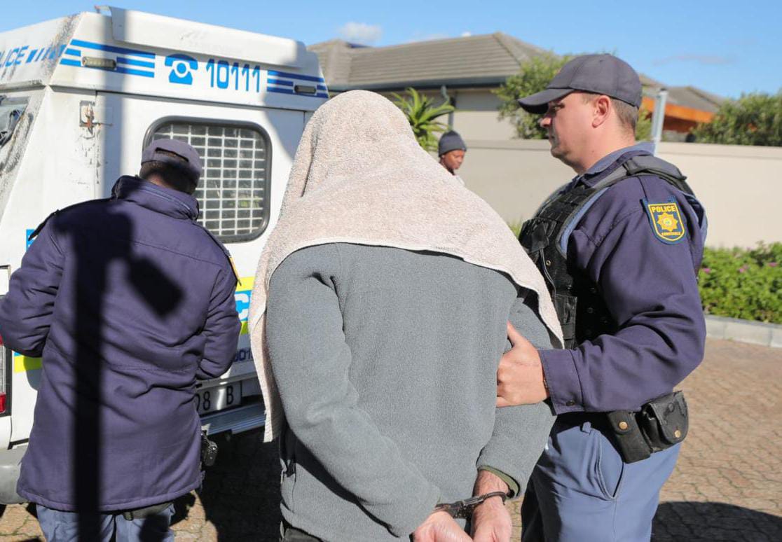 SAPS officers escorting a handcuffed suspect during an arrest operation in Bloubergstrand, Western Cape.