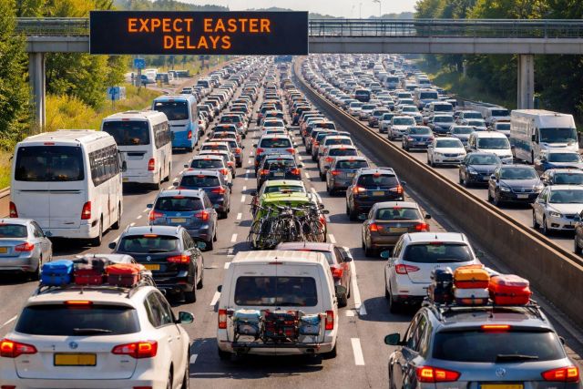 A high-volume South African motorway during the Easter holiday migration with an overhead gantry displaying "EXPECT EASTER DELAYS", highlighting the need for patience and behaviour change